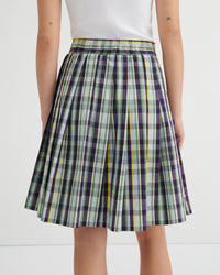 A pleated A-line skirt with a green, purple, and yellow plaid pattern, worn by a model with a white top against a plain white background.