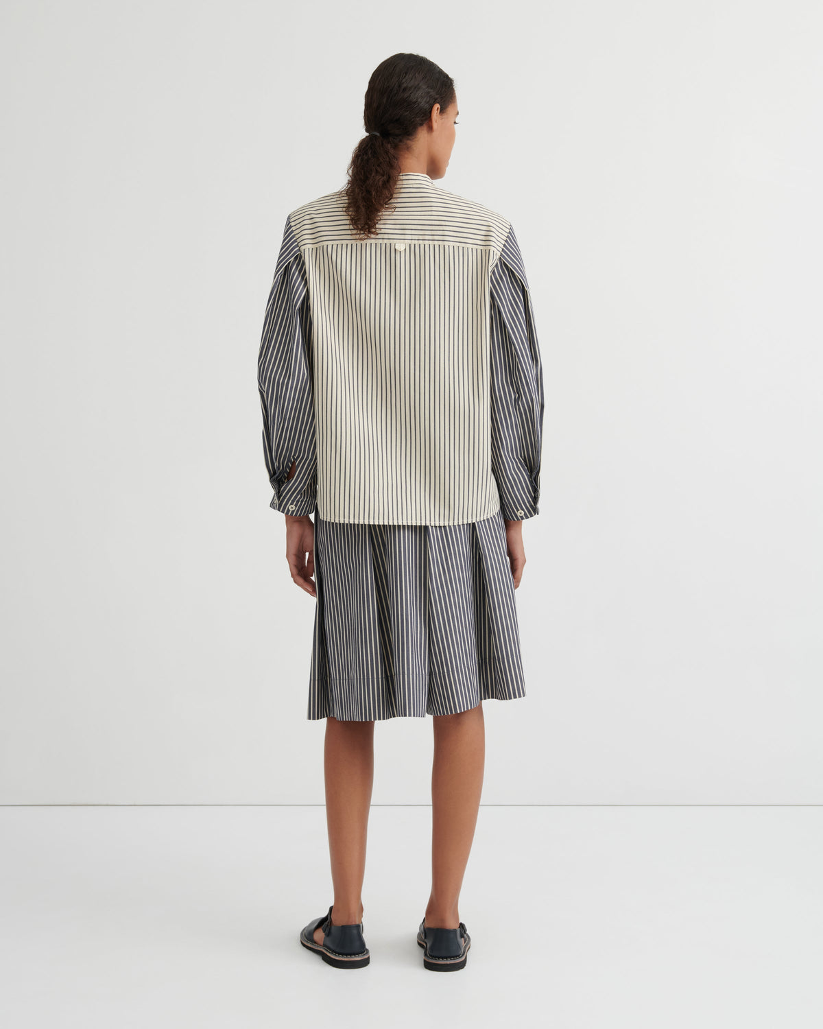 A model viewed from the back wearing a striped shirt and matching striped skirt in a studio setting.