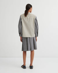 A model viewed from the back wearing a striped shirt and matching striped skirt in a studio setting.