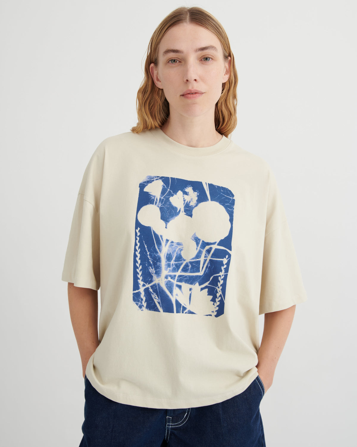 Person wearing a beige t-shirt with a blue and white graphic design on a plain background