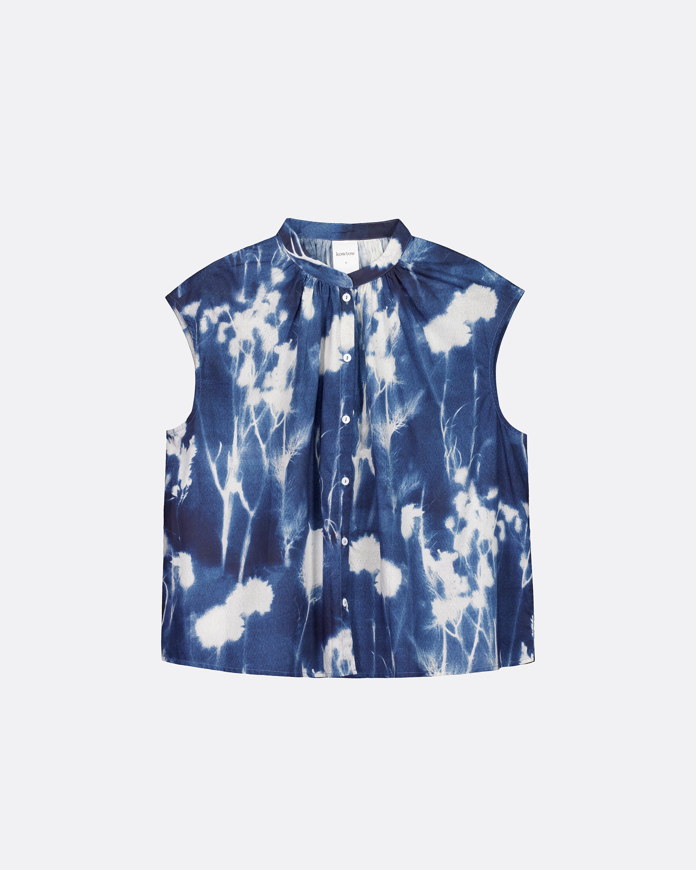 A sleeveless button-front top with a stand collar, featuring a blue and white cyanotype floral pattern, displayed flat against a light gray background.