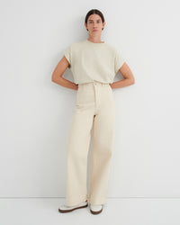 A woman modeling a light cream short-sleeve crewneck top and matching high-waisted wide-leg trousers, standing against a plain white studio wall.