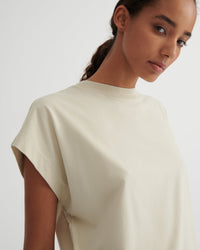 A close-up of a model wearing a cream-colored short-sleeve crewneck t-shirt against a plain light gray background.