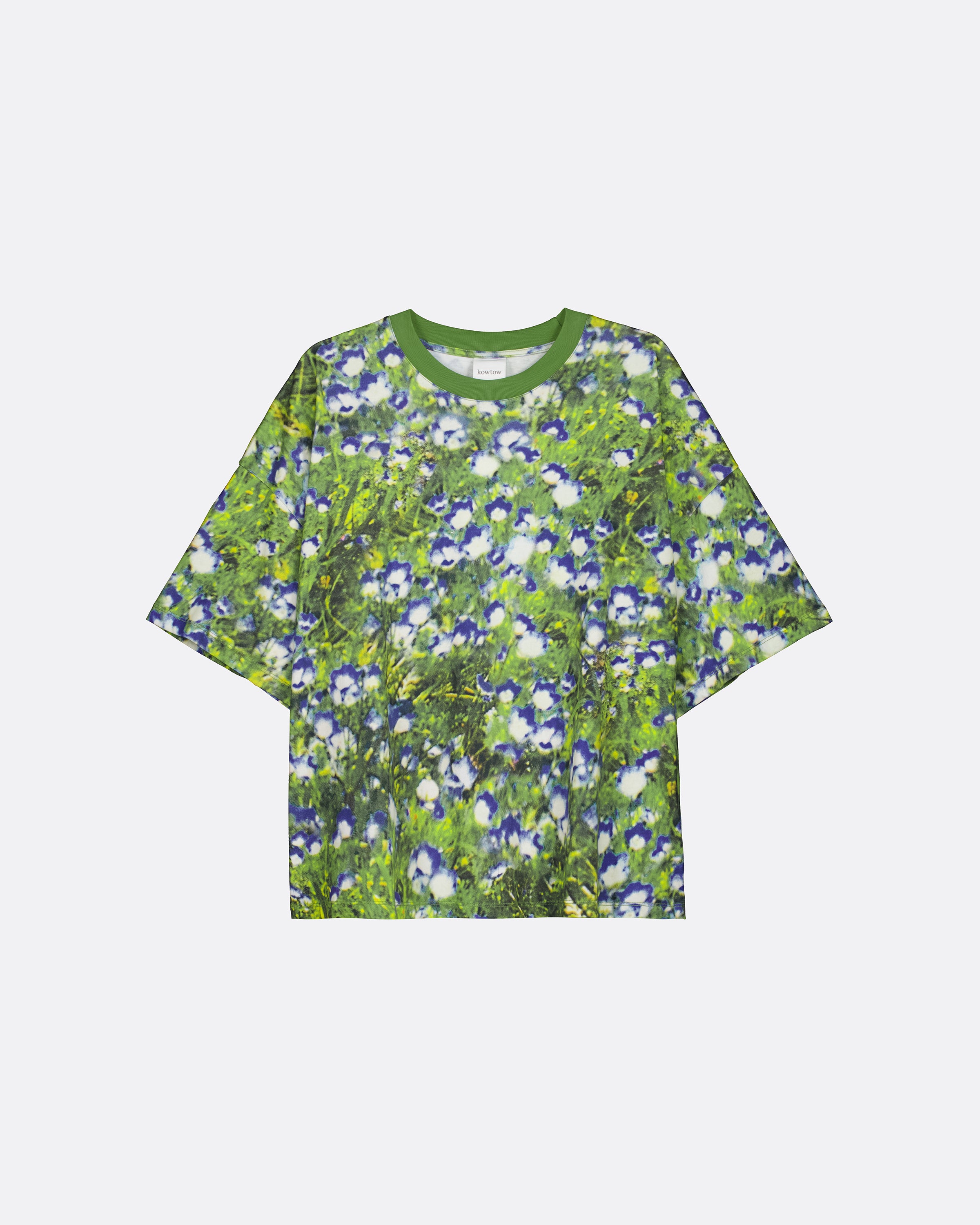 A short-sleeve crewneck t-shirt featuring an all-over floral print of blue and white flowers on a green background, displayed flat against a light gray studio backdrop.