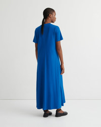 A woman wearing a bright blue short-sleeve maxi dress, shown from the back in a studio setting with a white background.