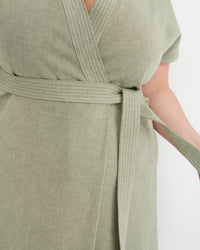 Close-up of a sage green wrap dress with a matching tie belt, featuring a textured linen-like fabric and subtle vertical stripe detailing.
