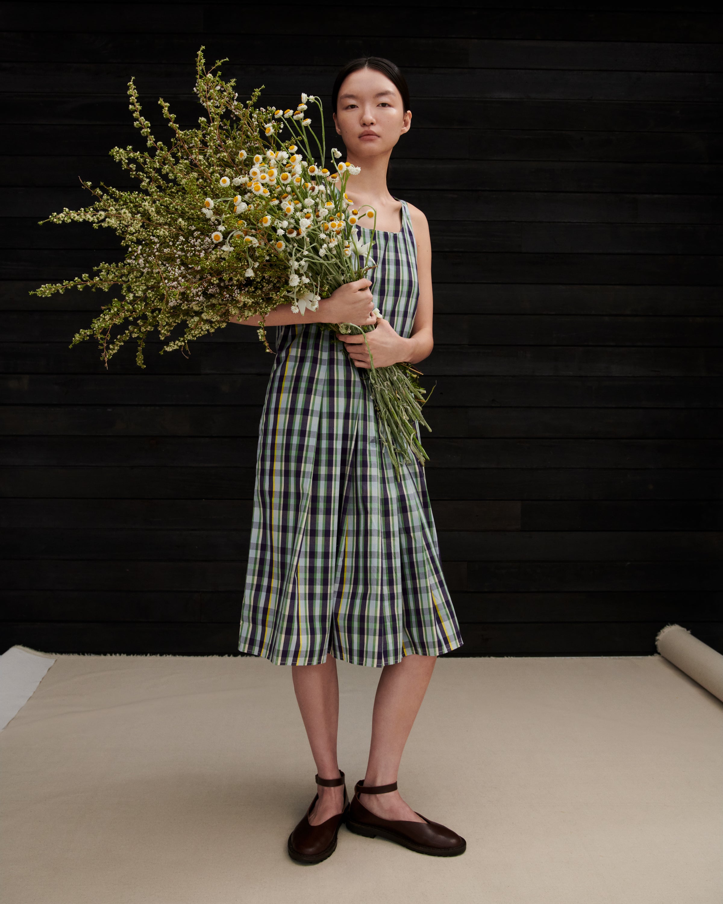 Woman in a checkered dress holding flowers against a black background
