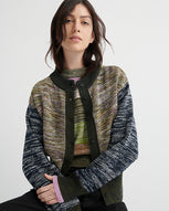 A women wears a patchwork cardigan over a patchwork vest with black jeans against a white backdrop.
