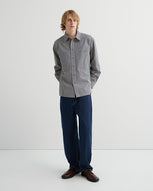 A man wears a check shirt and dark blue jeans stands against a white backdrop.