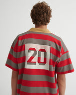 A man stands in front of a white wall with his back to the camera, wearing a rugby red and grey striped shirt with the number 20 on the back.