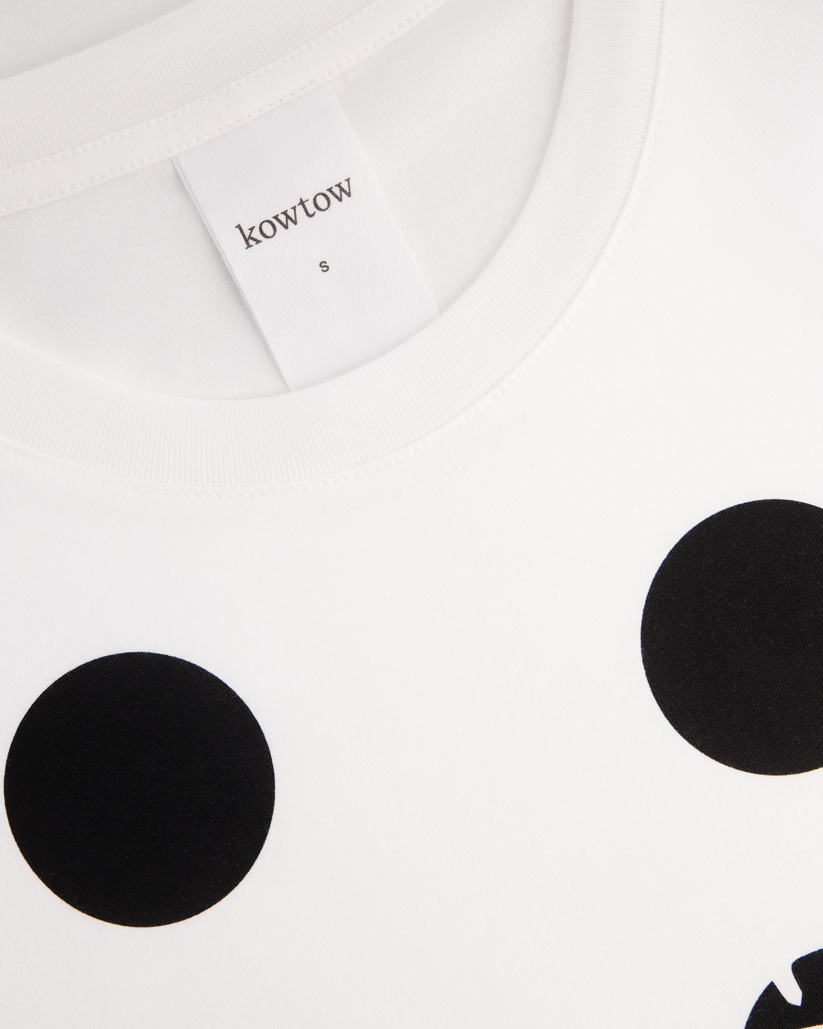 Close-up of a white crewneck t-shirt with black polka dots, showing the inner neck label with the brand name 'kowtow'.