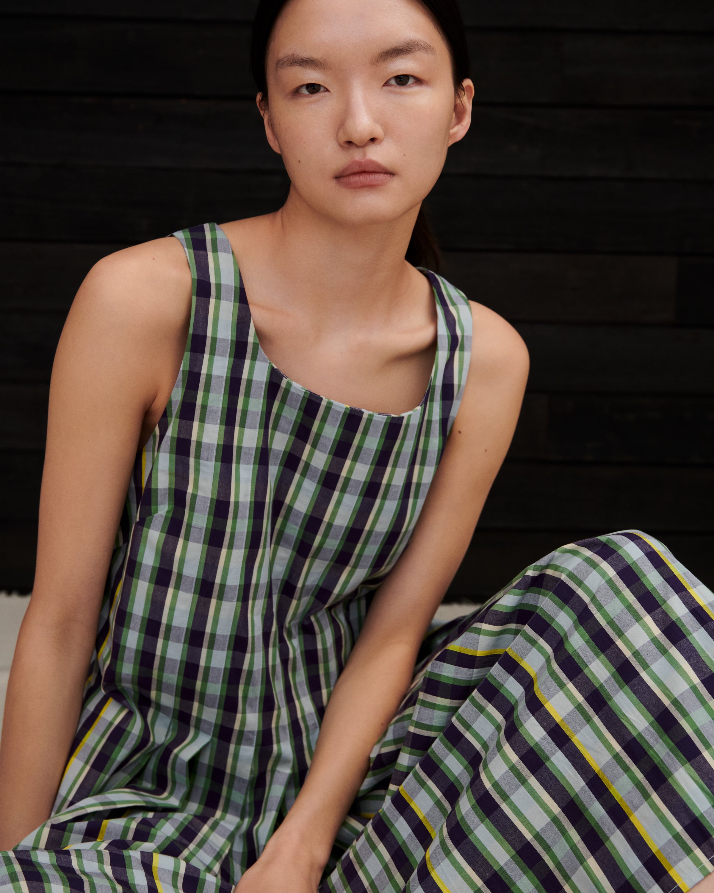 Woman wearing a green and purple checkered dress sitting against a dark wooden background