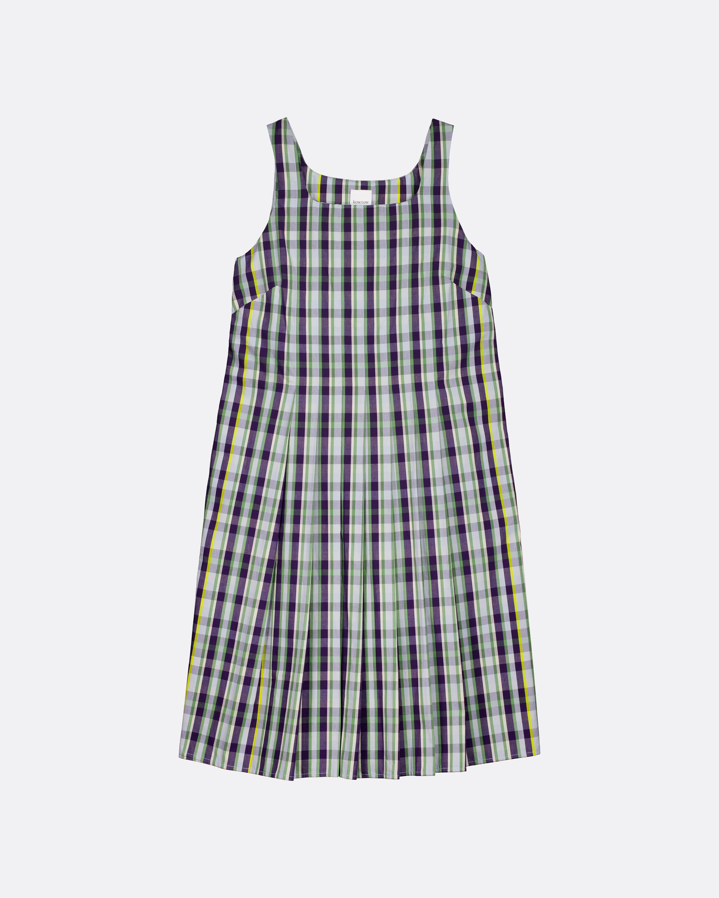 A sleeveless plaid pinafore dress with a white base and black, green, and yellow stripes, shown flat on a light gray background.