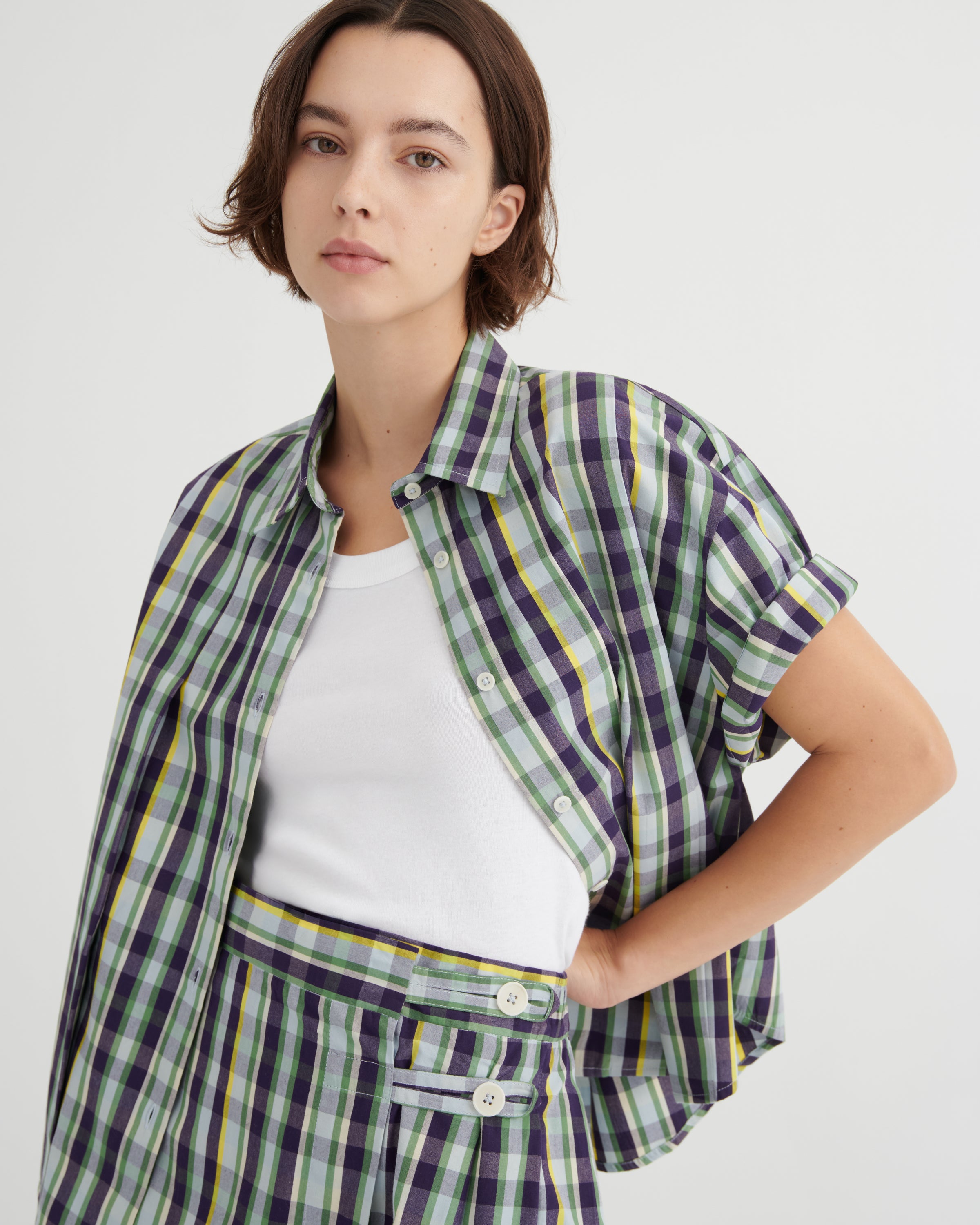 Woman wearing a plaid shirt over a white top with a plain background