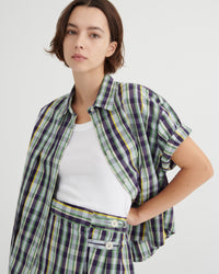 Woman wearing a plaid shirt over a white top with a plain background