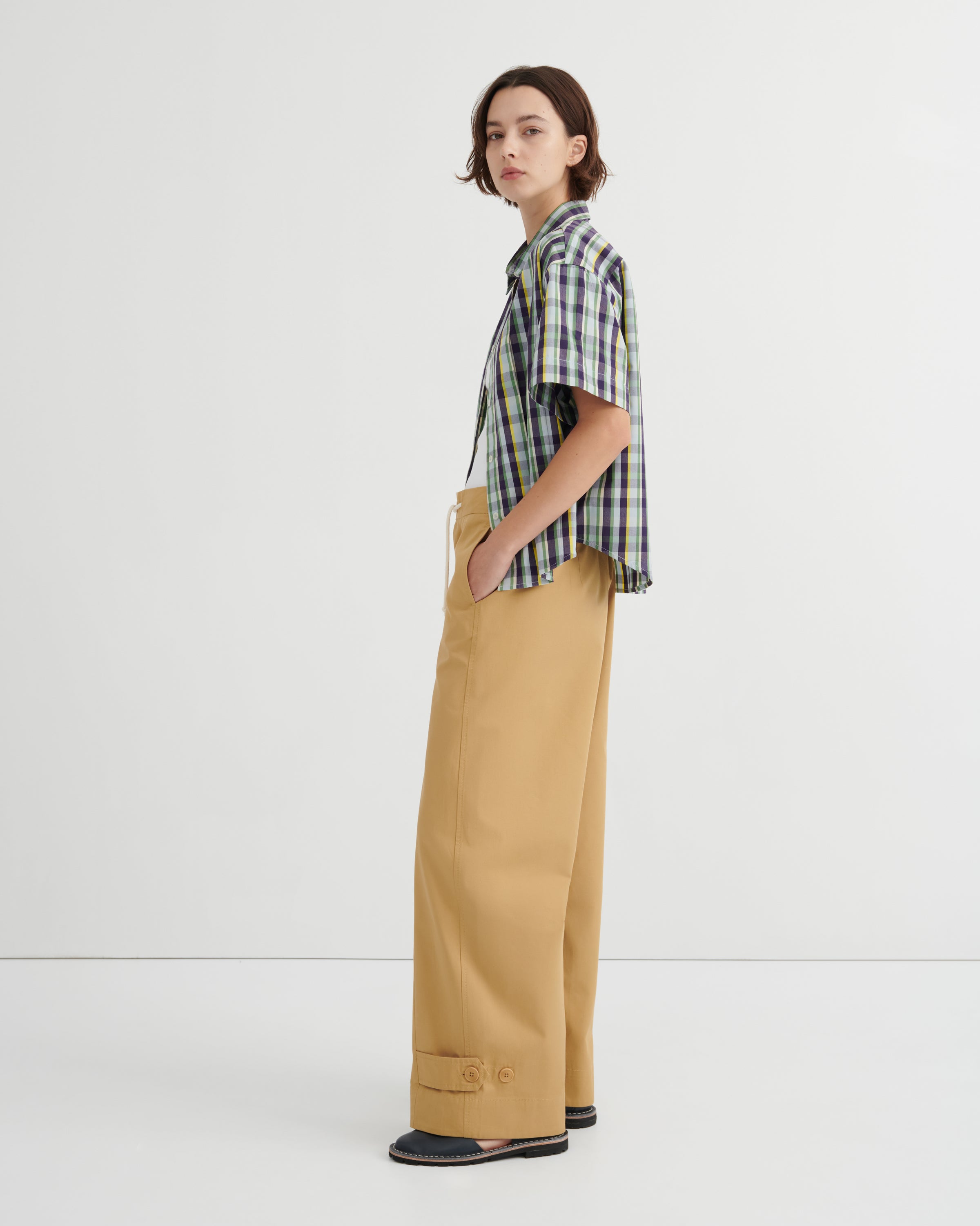 Person wearing a plaid shirt and beige pants on a white background