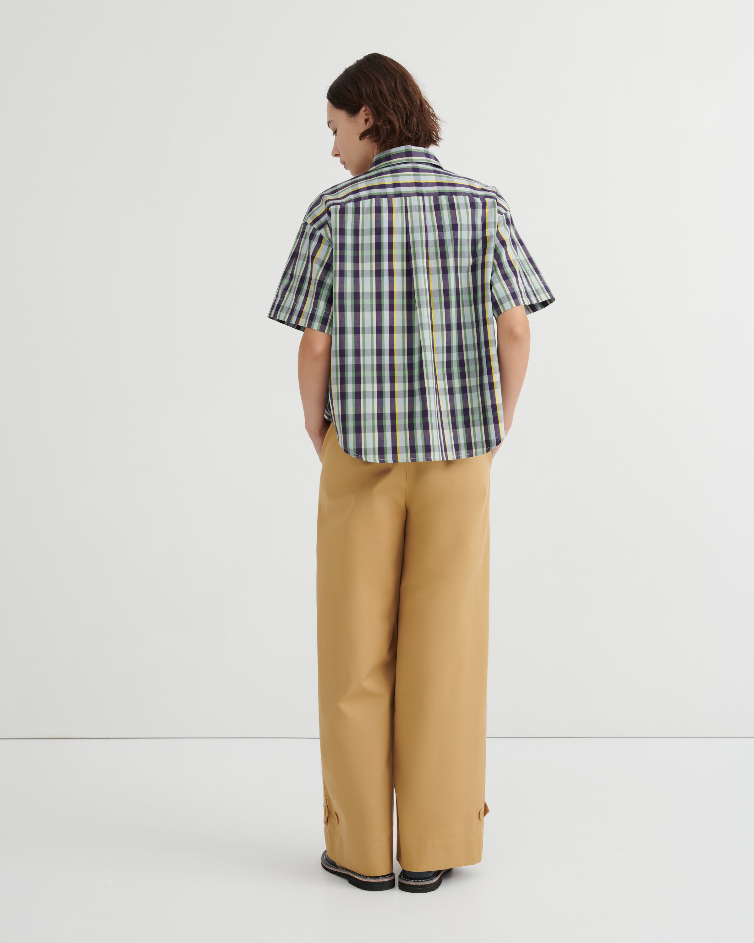 Person wearing a plaid shirt and beige pants on a white background