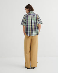 Person wearing a plaid shirt and beige pants on a white background