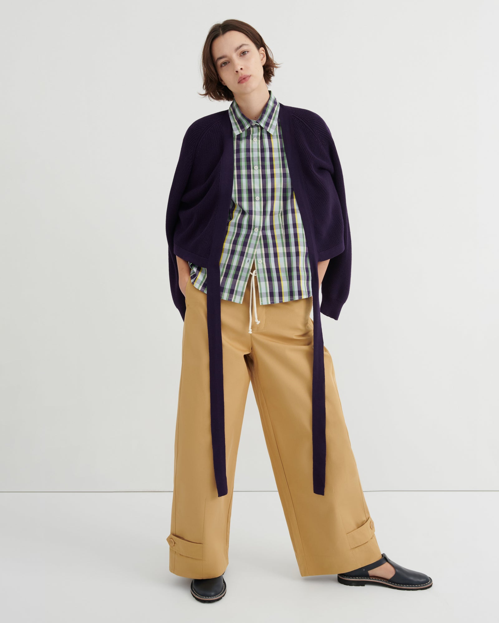 Person wearing a plaid shirt, navy cardigan, and beige pants on a white background