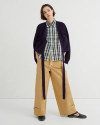 Person wearing a plaid shirt, navy cardigan, and beige pants on a white background
