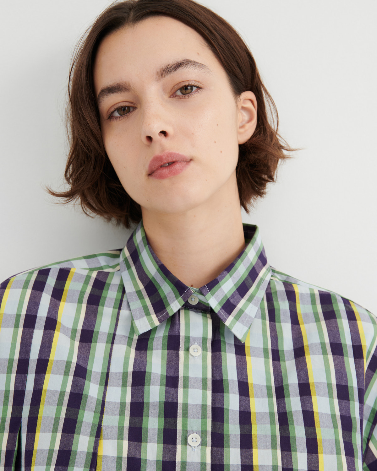Person wearing a green and purple plaid shirt against a white background