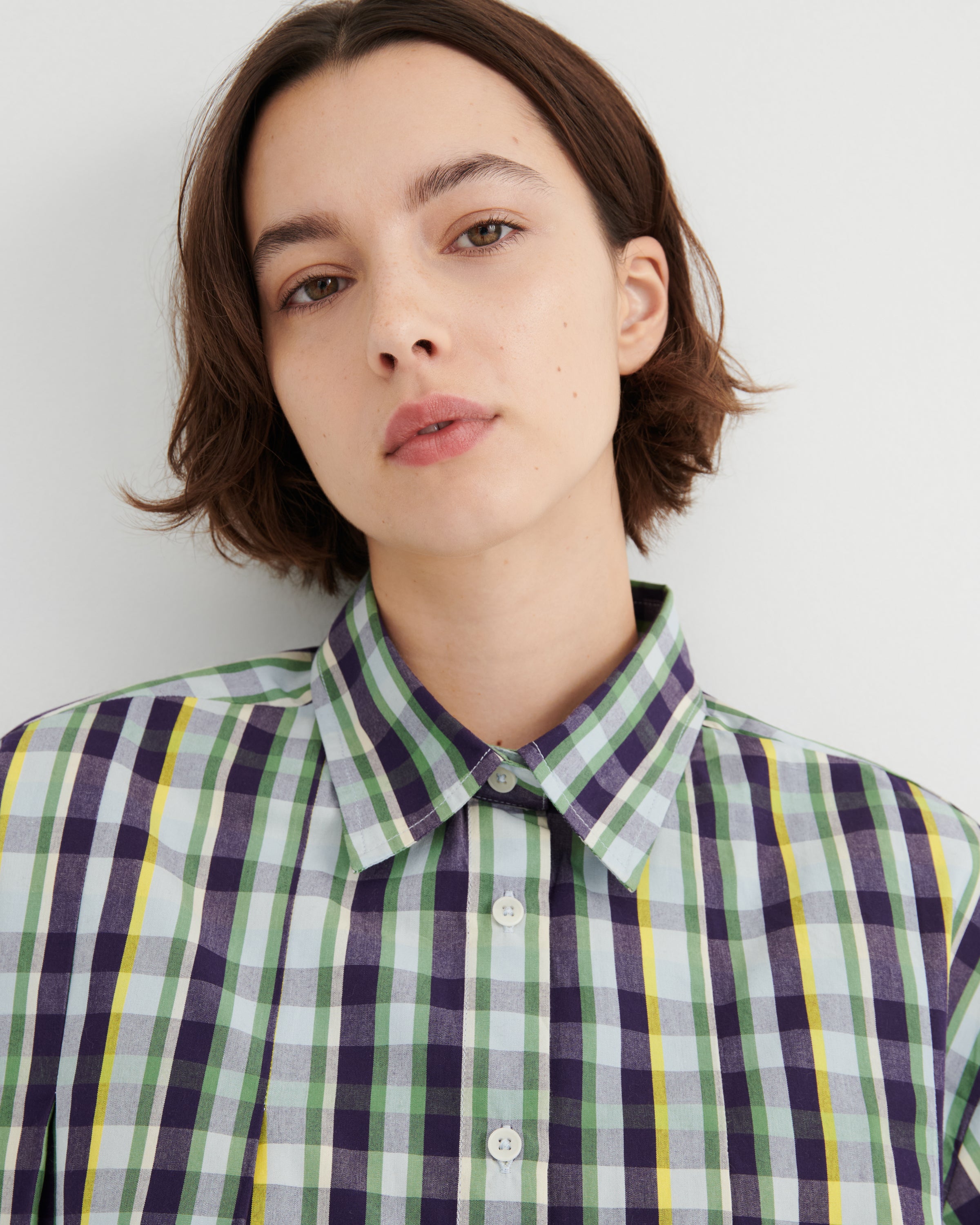 Person wearing a green and purple plaid shirt against a white background