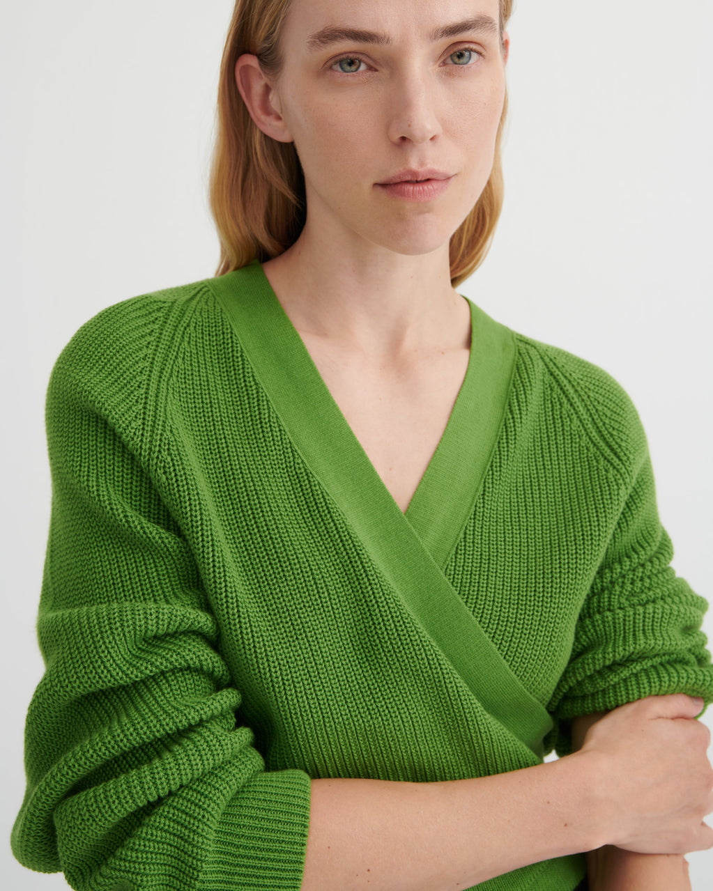 A close-up of a woman wearing a bright green ribbed knit V-neck wrap sweater, showing the texture and fit against a plain light background.