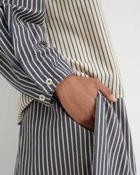 Close-up of a person wearing a navy and cream vertically striped shirt and matching striped trousers, with one hand tucked into a pocket.