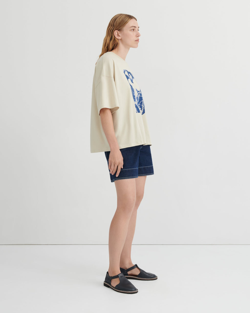 Woman wearing a beige t-shirt with a graphic design and denim shorts on a white background