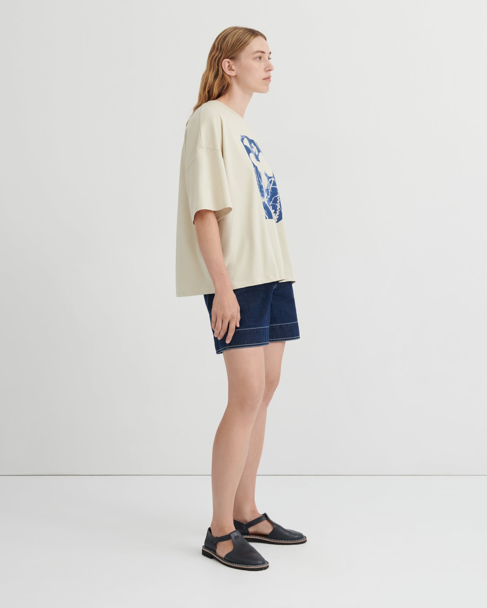 Woman wearing a beige t-shirt with a graphic design and denim shorts on a white background