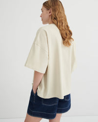 Person wearing a cream oversized shirt and denim shorts on a white background