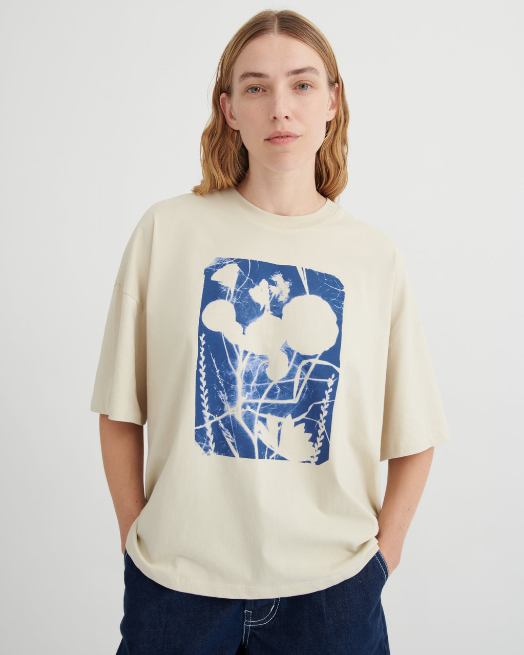 Person wearing a beige t-shirt with a blue and white graphic design on a plain background