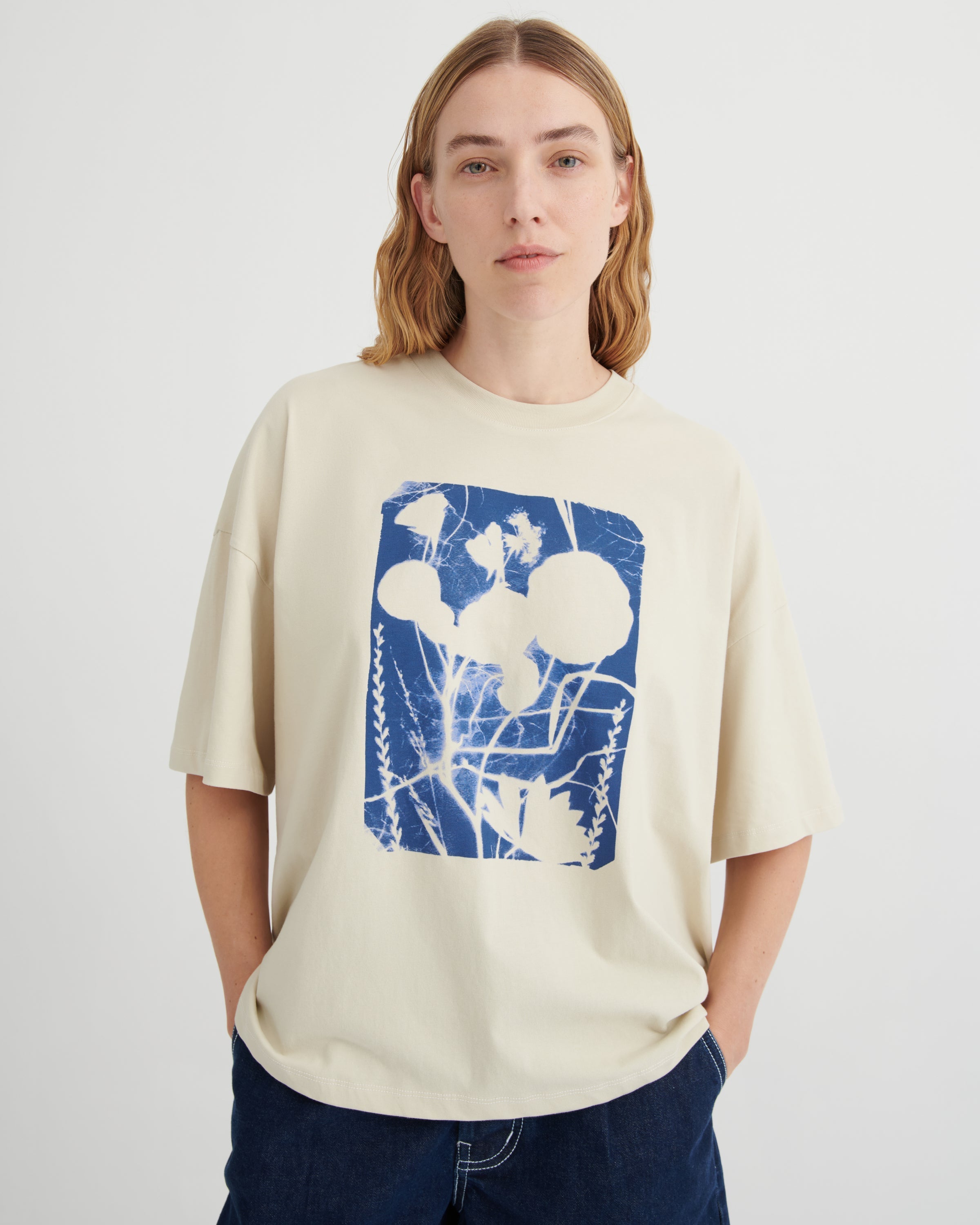 Person wearing a beige t-shirt with a blue and white graphic design on a plain background