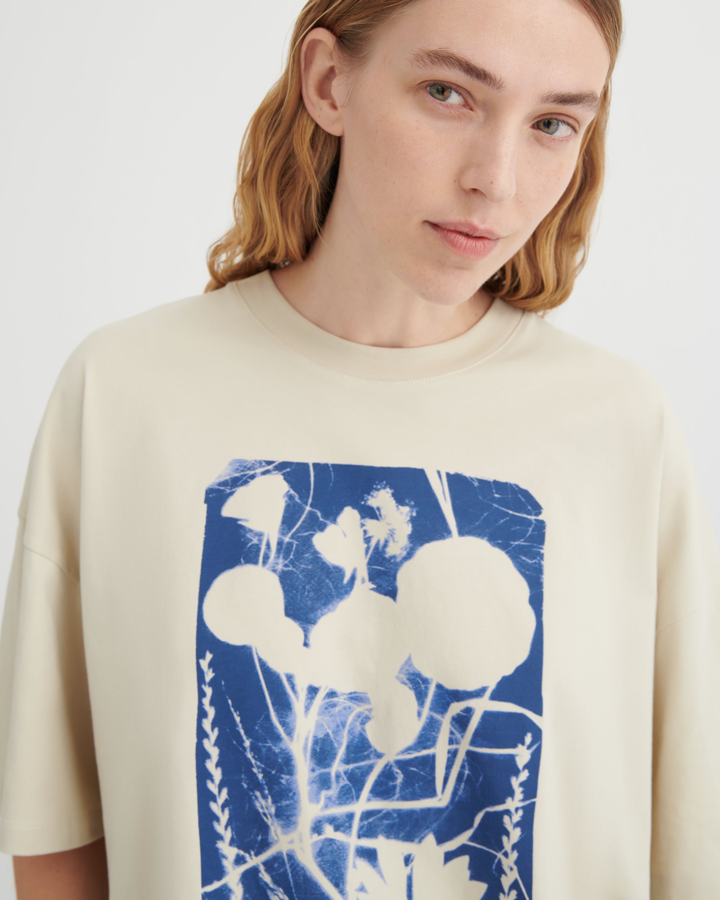 Person wearing a beige t-shirt with a blue and white abstract design on a plain background