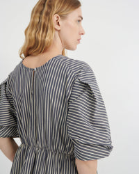 A woman shown from the back wearing a dark gray and white vertically striped dress with puff sleeves and a gathered waist, photographed against a clean white studio background.