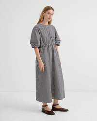 A woman modeling a loose-fitting midi dress with vertical black and white stripes, short puff sleeves, and a gathered waist, paired with dark brown flat shoes against a plain white studio background.