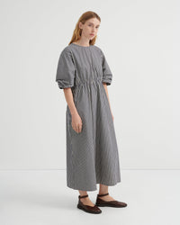 A woman modeling a loose-fitting midi dress with vertical black and white stripes, short puff sleeves, and a gathered waist, paired with dark brown flat shoes against a plain white studio background.