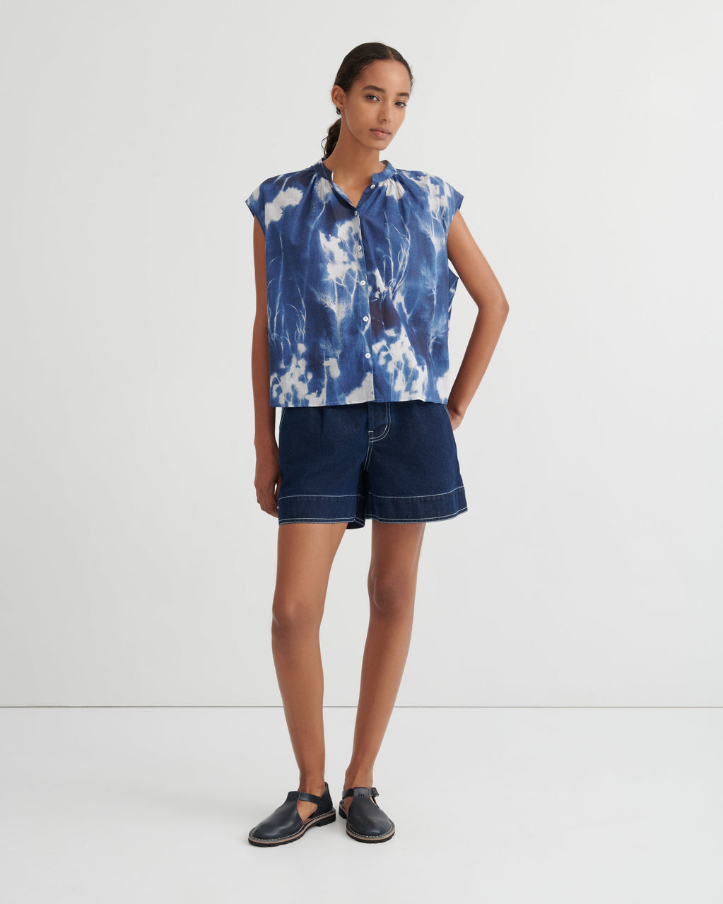 Woman wearing a blue tie-dye top and denim shorts on a white background