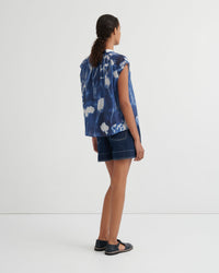 Woman wearing a blue tie-dye shirt and denim shorts on a white background