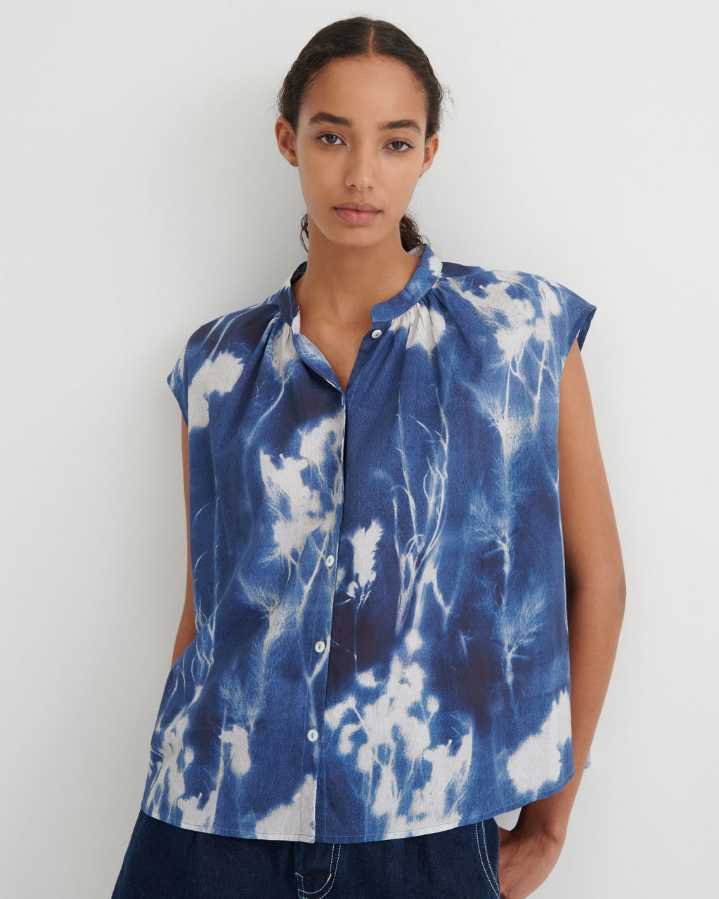 Woman wearing a blue and white tie-dye sleeveless blouse against a white background