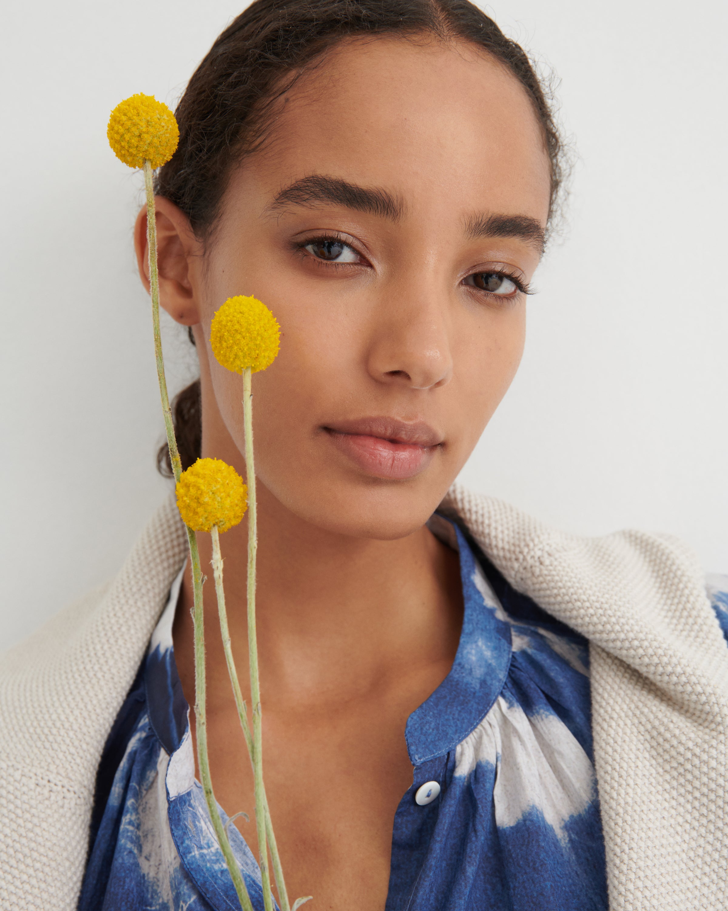 Woman with yellow flowers near her face against a white background
