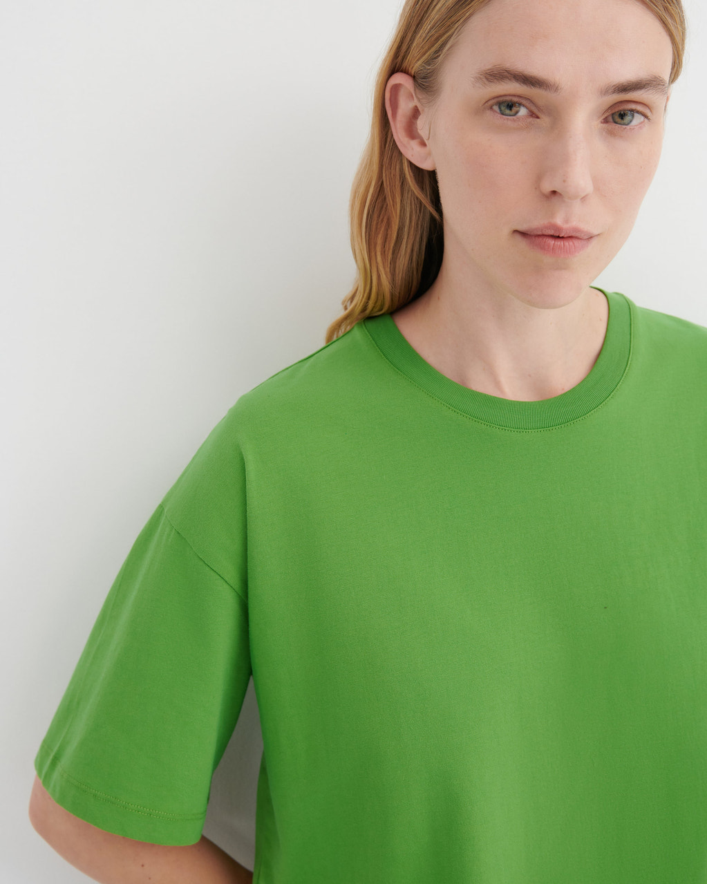 A close-up of a model wearing a bright green crewneck t-shirt against a plain light gray background.