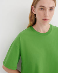 A close-up of a model wearing a bright green crewneck t-shirt against a plain light gray background.