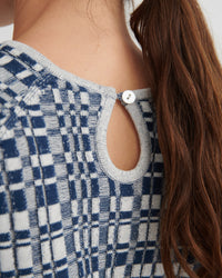 Close-up of the back of a person wearing a blue and white plaid knit top with a keyhole cutout and a white button.