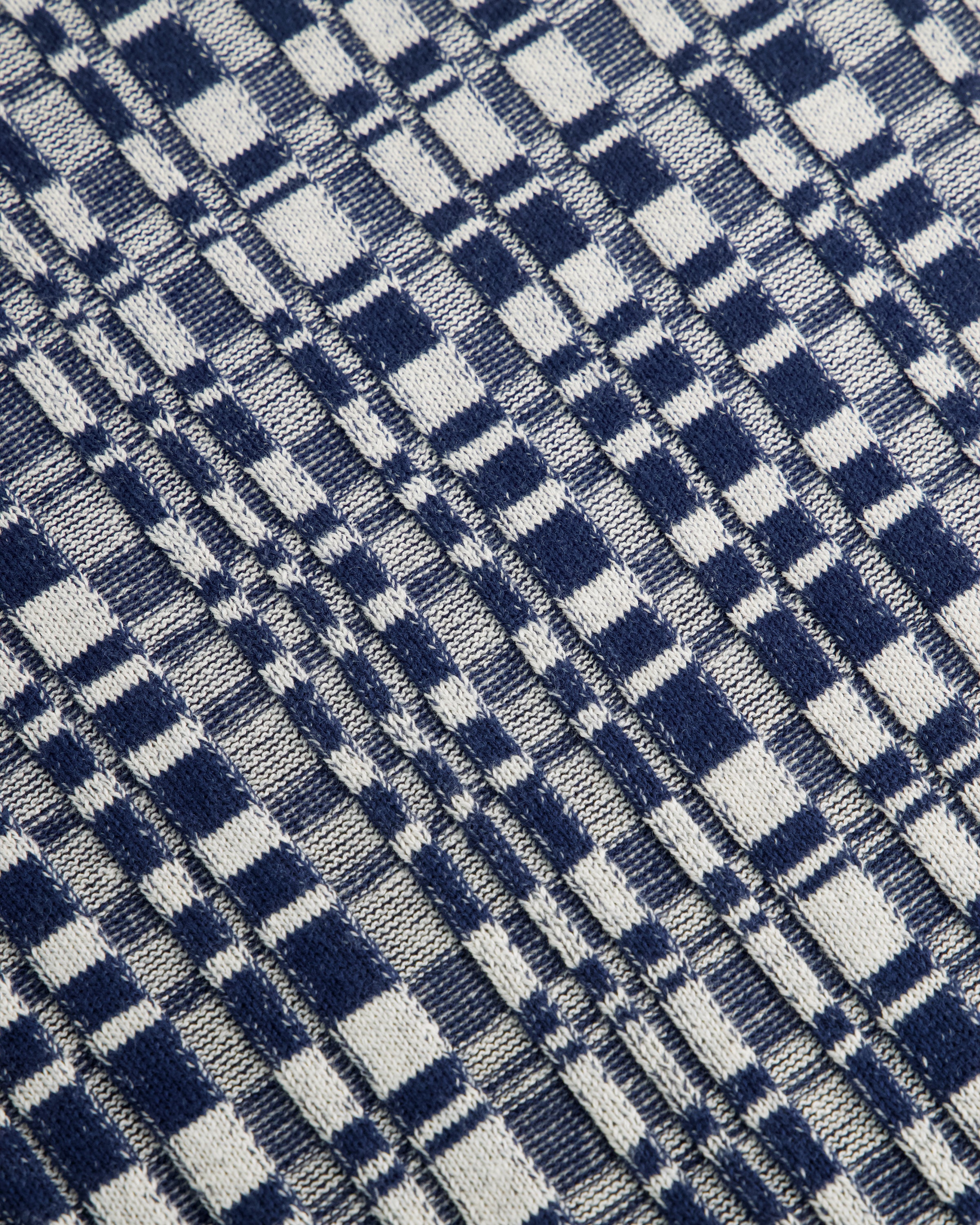 A close-up of a woven fabric with a navy blue and off-white plaid pattern, showing the texture of the material.
