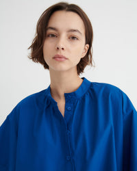 A woman with short brown hair wearing a vibrant royal blue button-up dress.