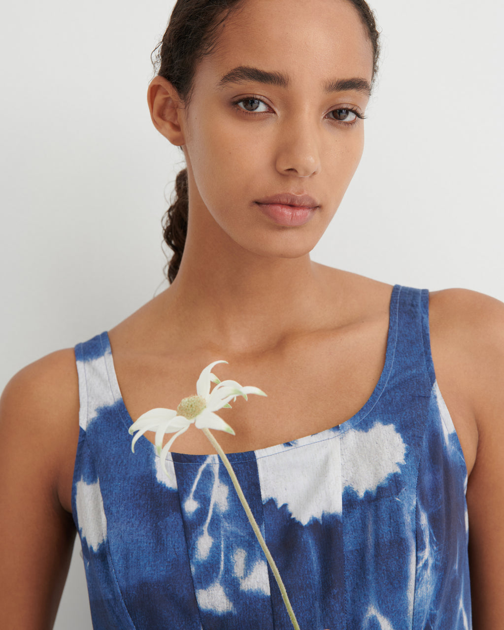 Woman wearing a blue and white tie-dye dress holding a white flower.