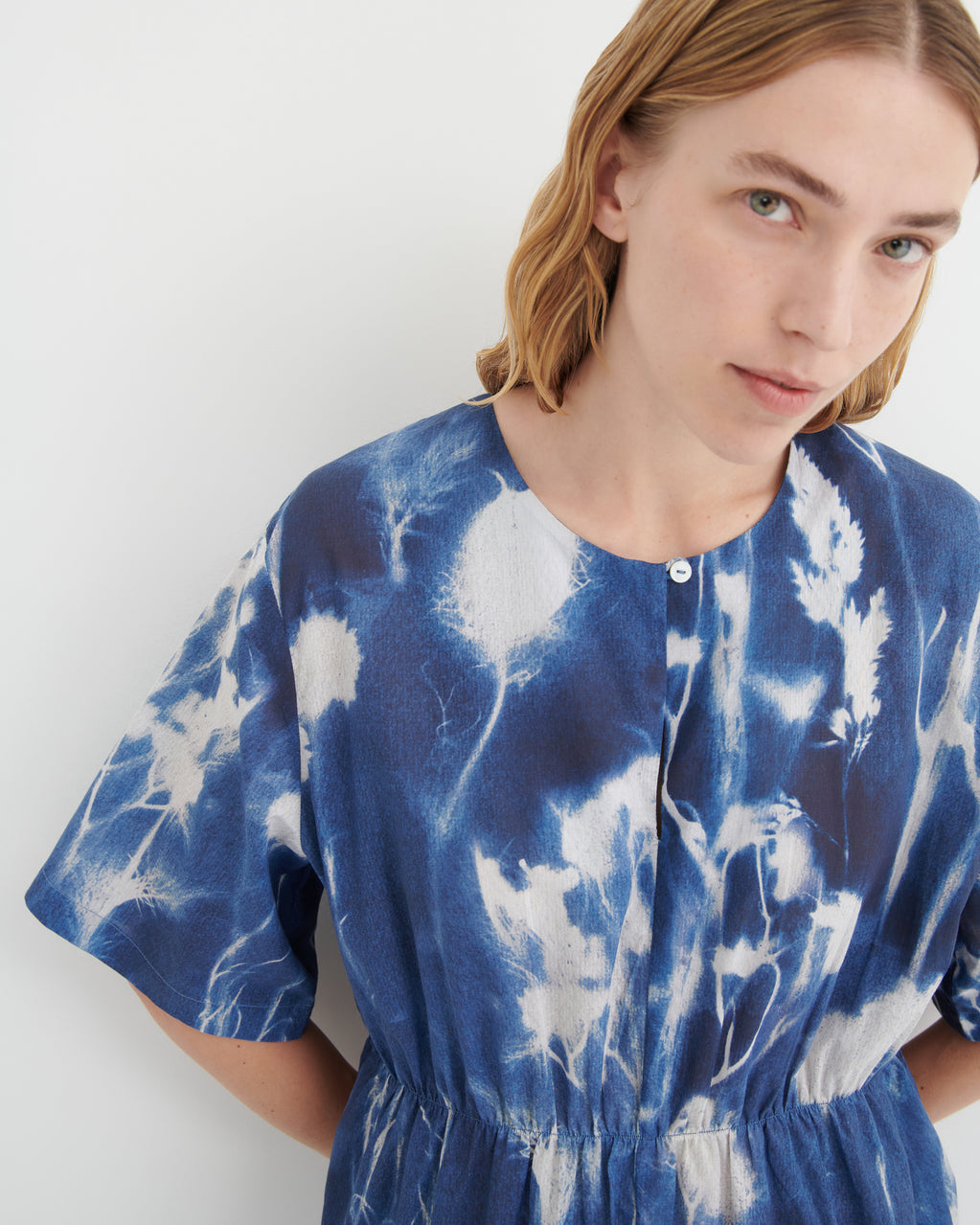 A close-up of a model wearing a blue and white tie-dye short-sleeve top with a buttoned neckline and gathered waist.