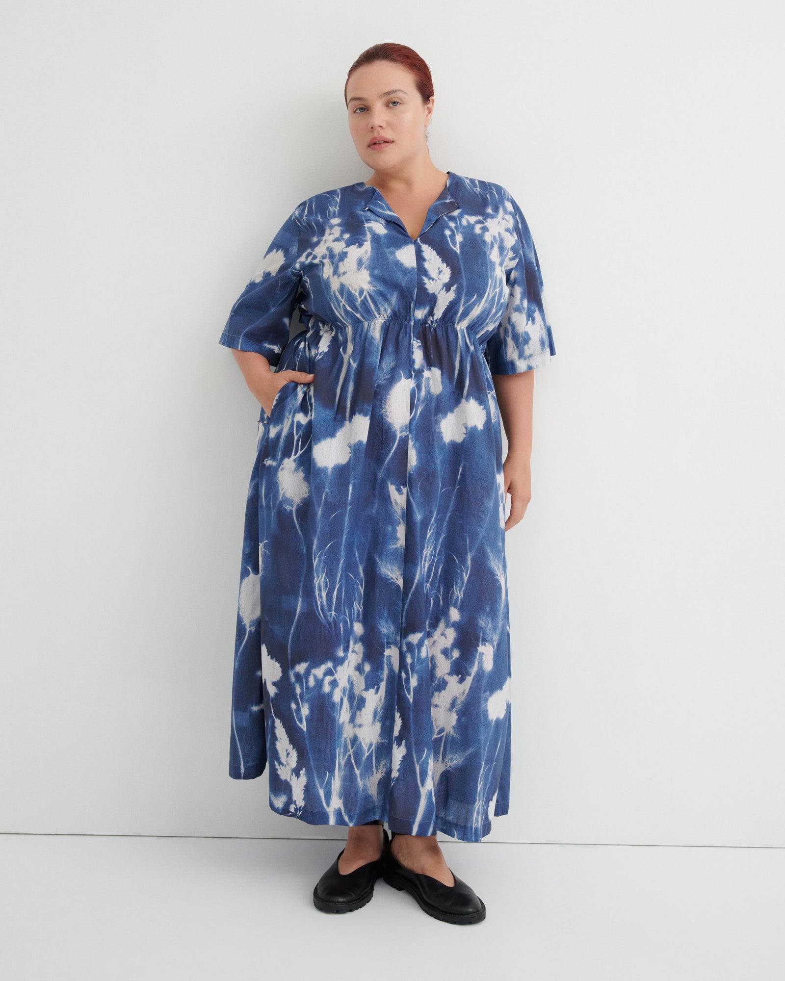 A woman modeling a blue and white tie-dye maxi dress with short flutter sleeves, a V-neck, and a drawstring waist, standing against a plain white studio background.