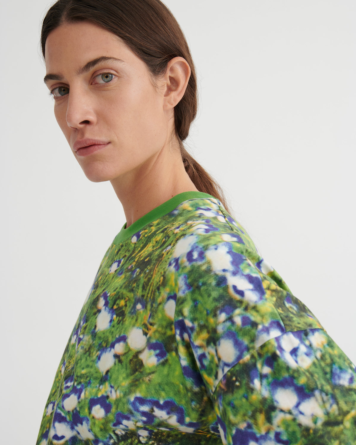 A woman wearing a green crewneck top with a blue, purple, and white floral print, photographed against a plain light gray background.
